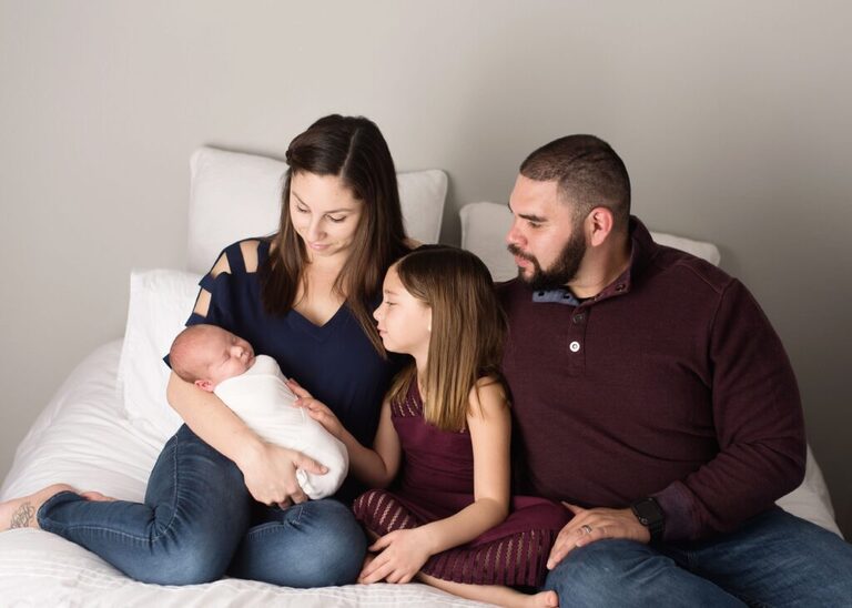 family-admire-newborn-posed-on-bed